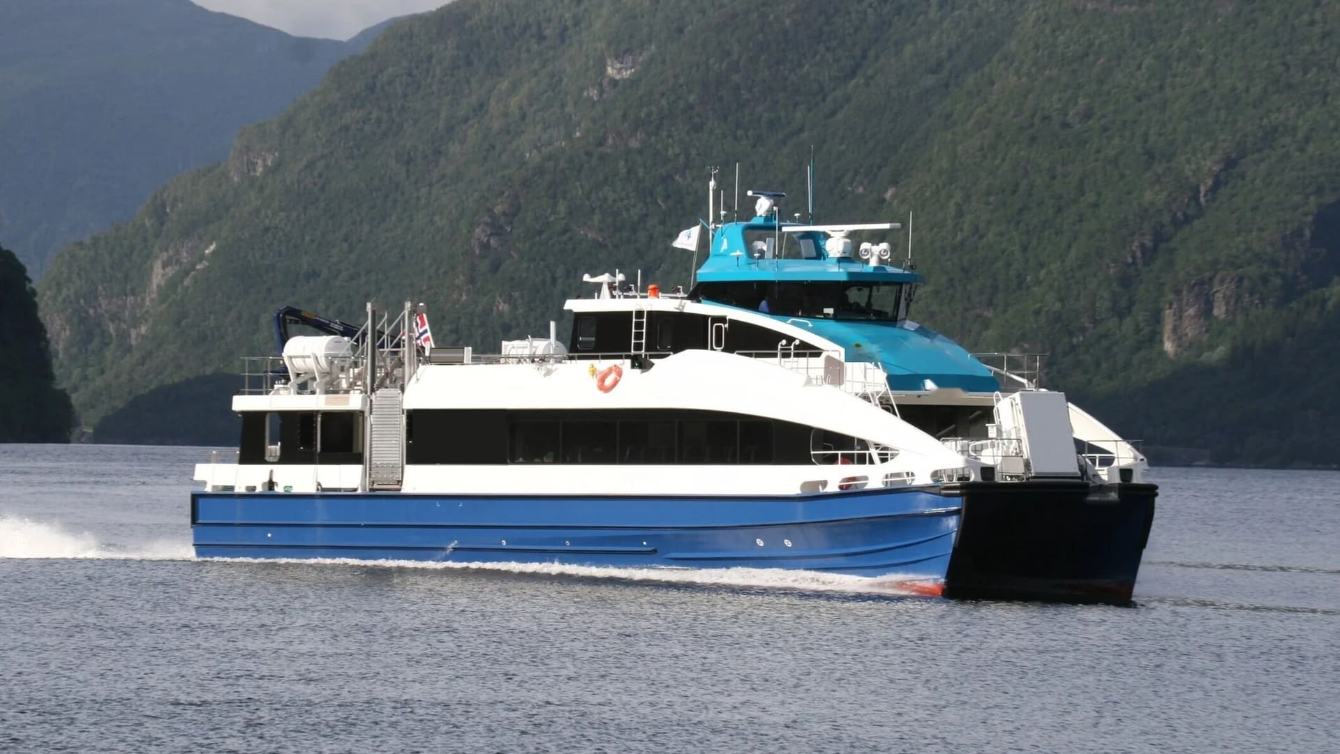 OBLUE FERRY 30 underway with bow spray, steep fjord slopes behind